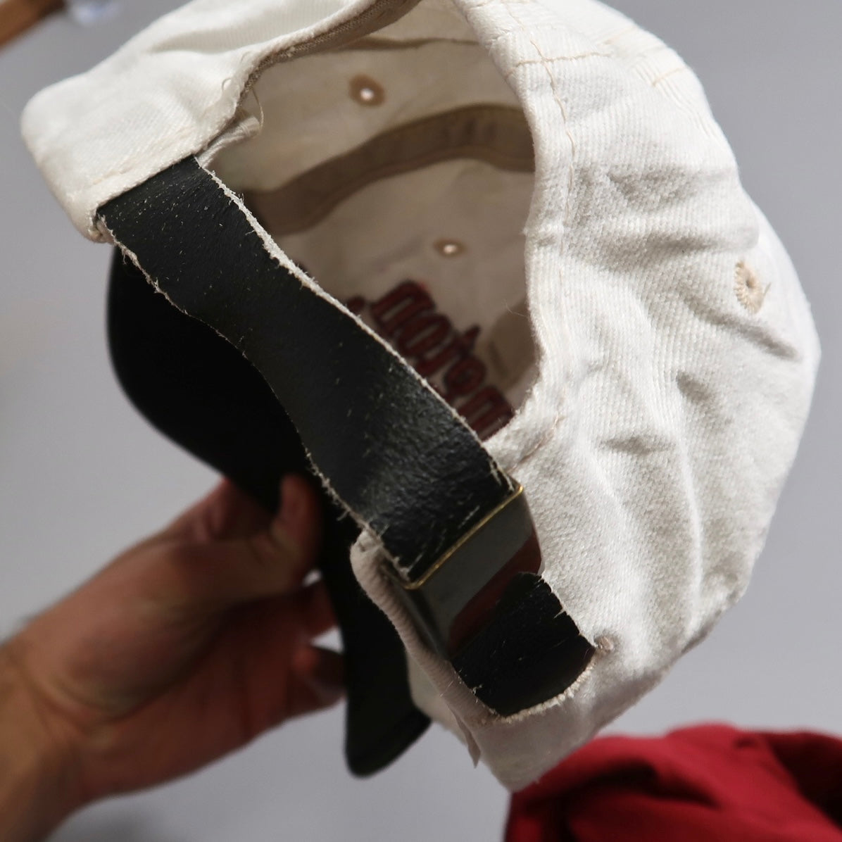 Back view of a white cap with a leather strap adjustment.