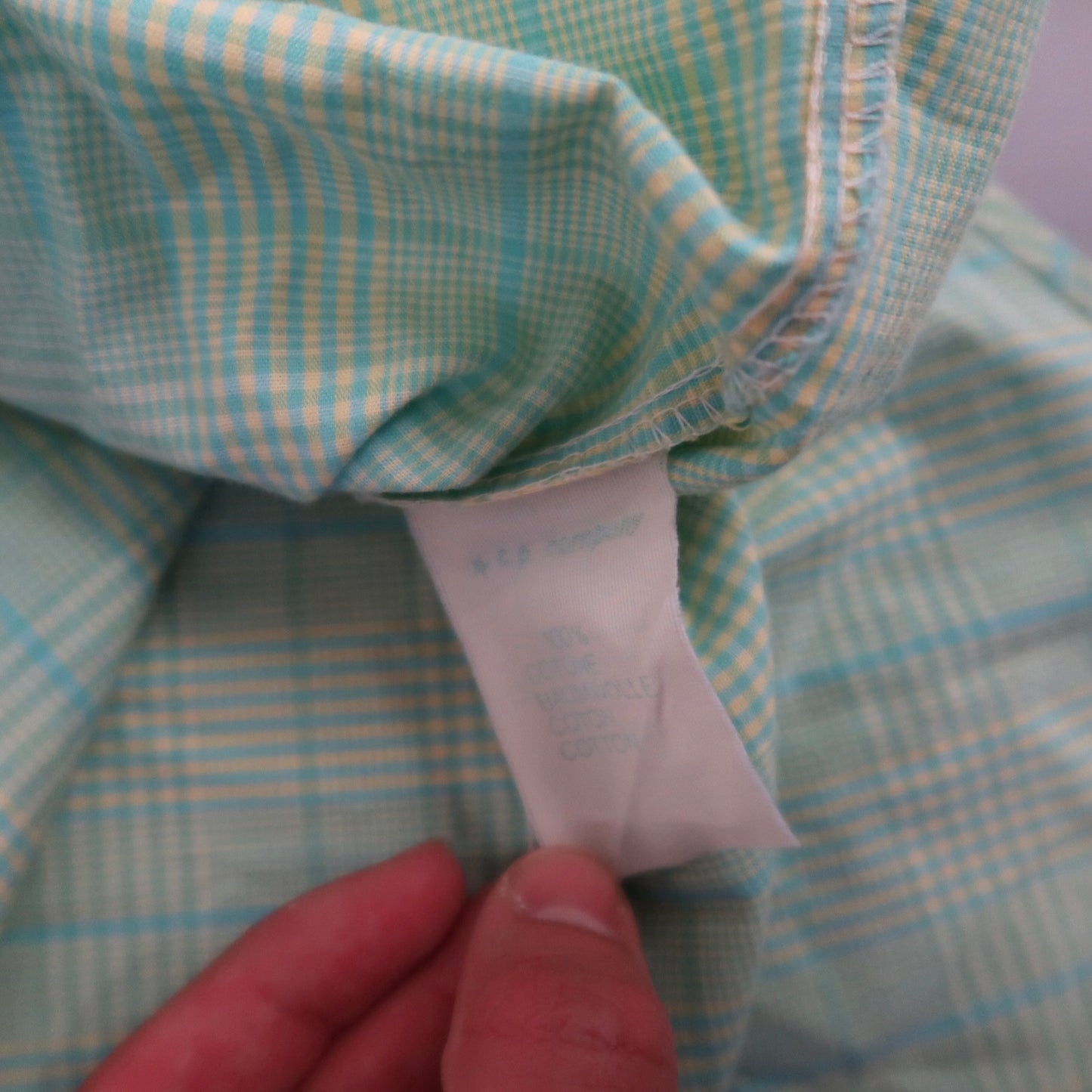Hand holding a clothing label on a green plaid fabric.