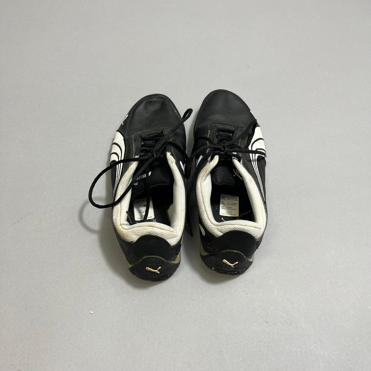 Black and white athletic shoes with laces on a gray surface.