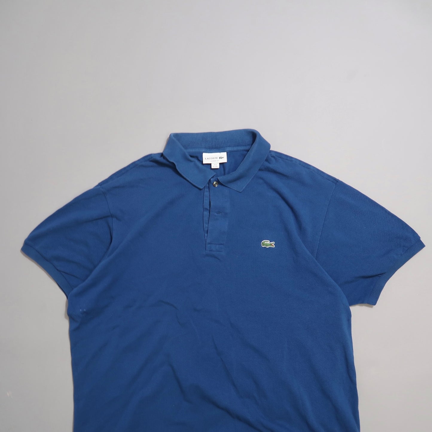 Blue polo shirt with a green logo on a plain background.