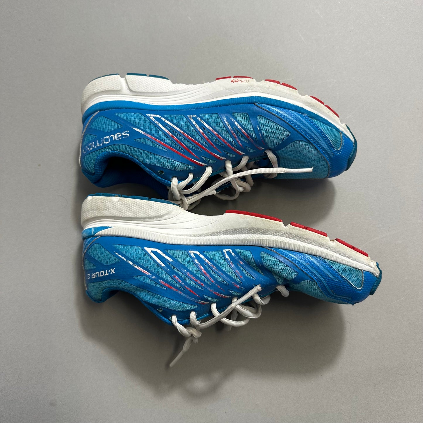 Blue running shoes with white and red details on a grey background.