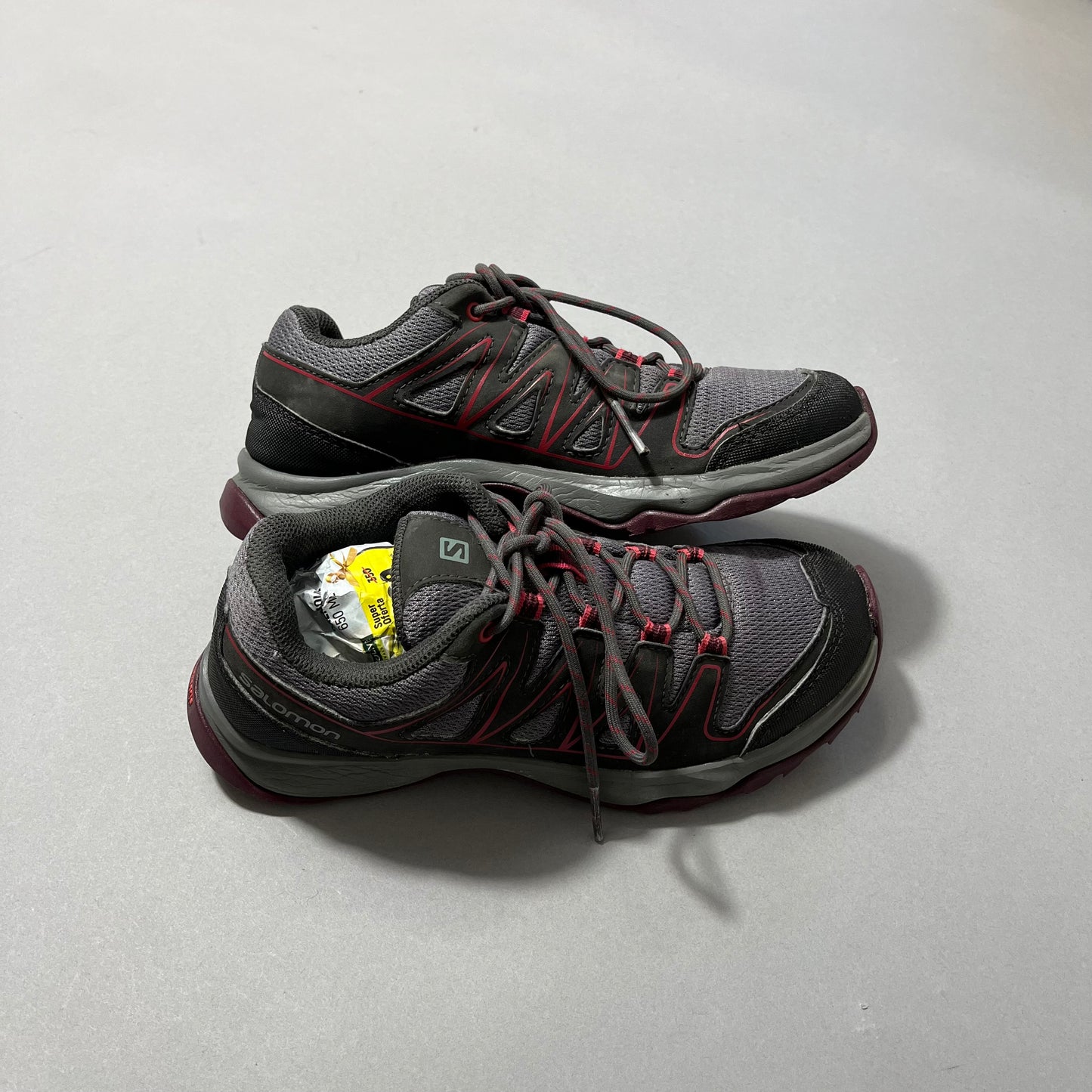 Gray and red trail shoes on a gray surface, one filled with paper.