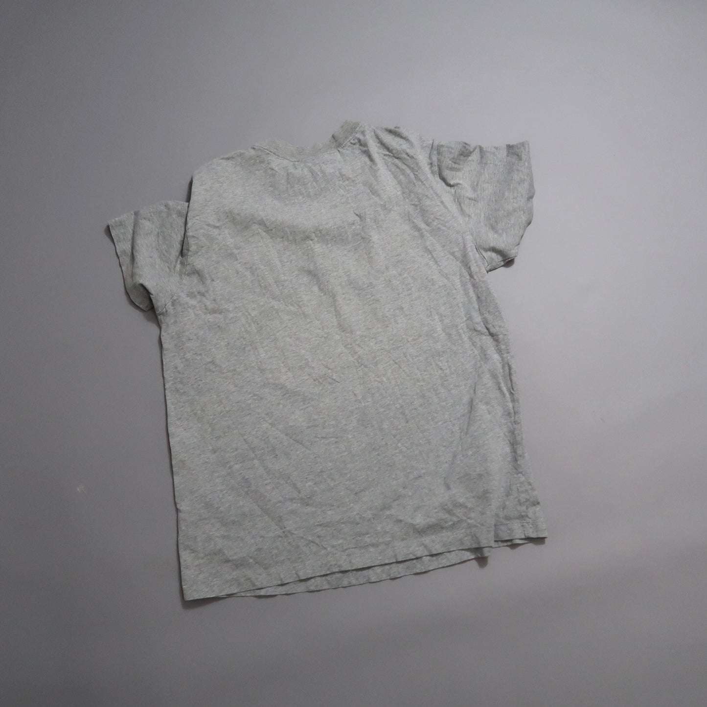 Wrinkled gray t-shirt laid flat on a plain surface.