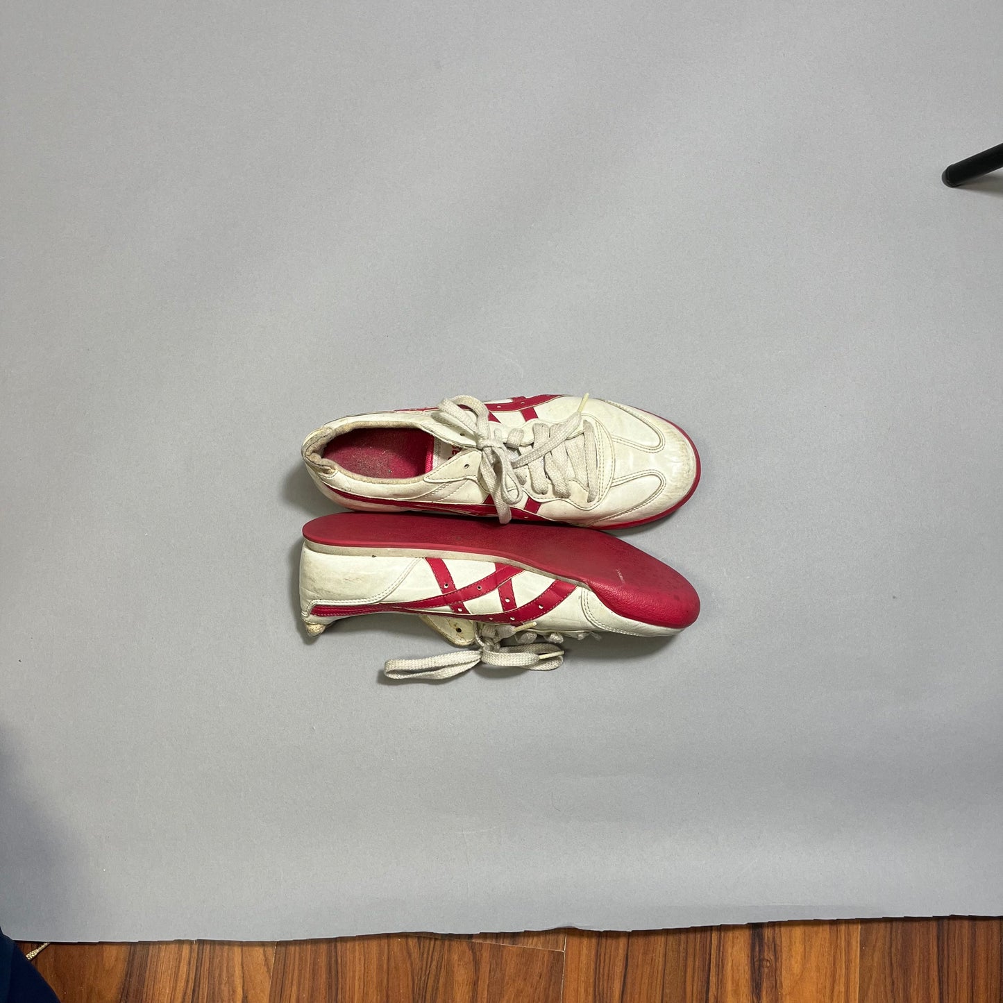 White and red sneakers on a gray background, wooden floor visible.