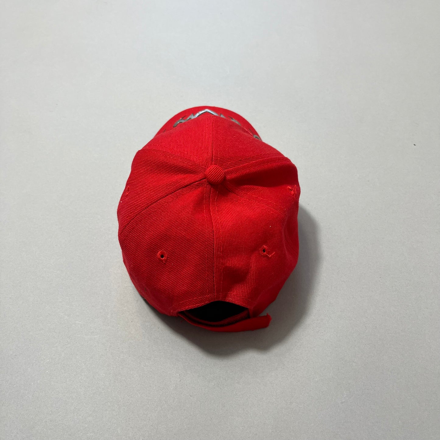 Red baseball cap lying on a gray surface, viewed from the back.