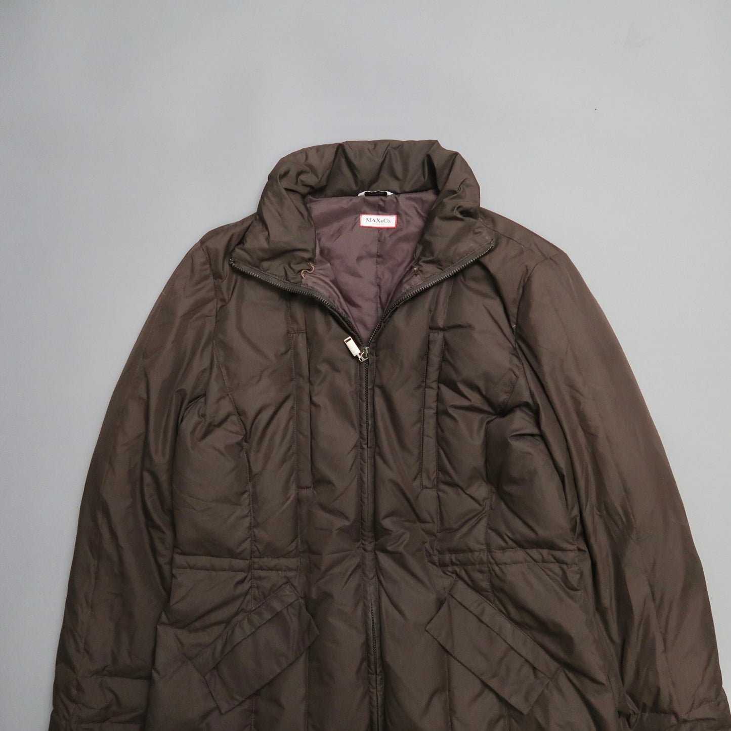 Brown puffer jacket with high collar and front zipper on gray background.
