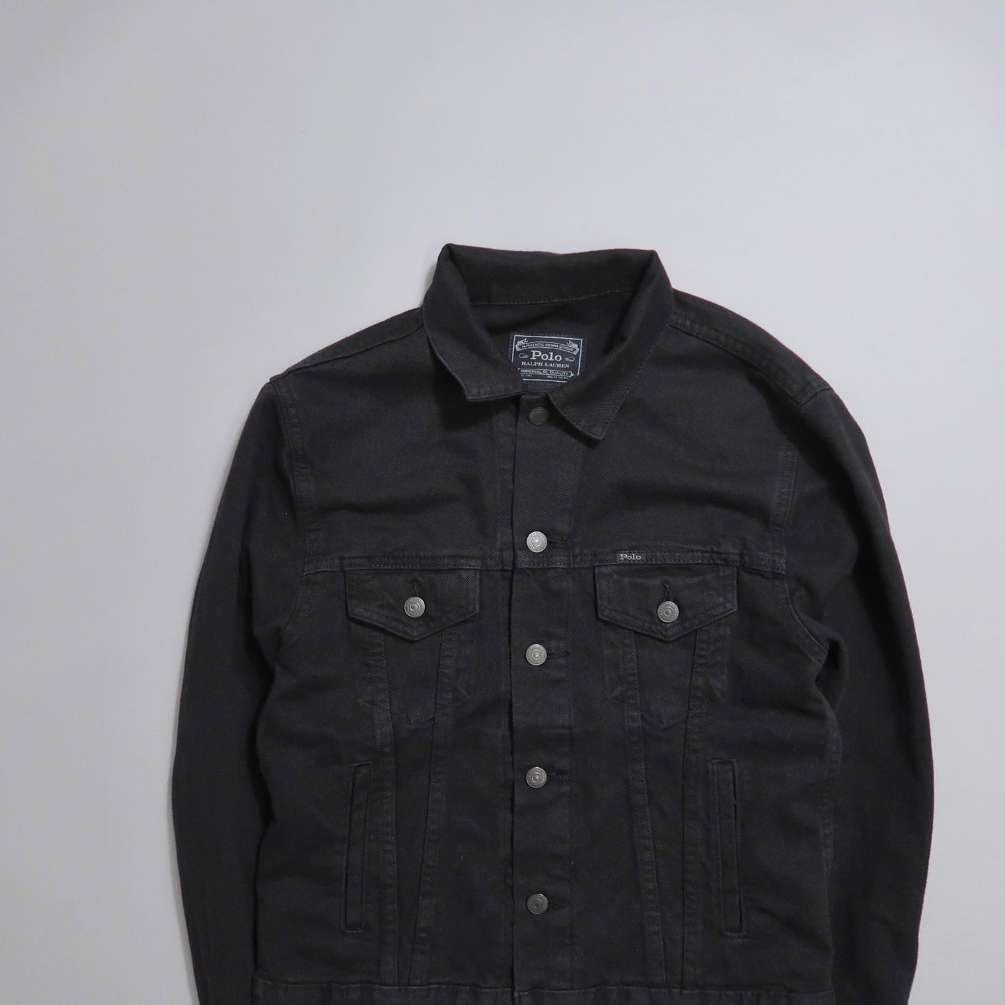 Black denim jacket with button details, laid flat.