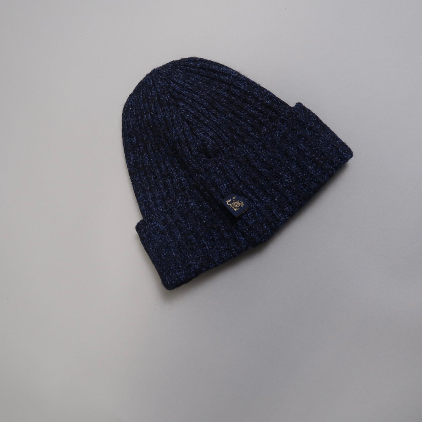 Dark blue knitted beanie hat on a light gray background.