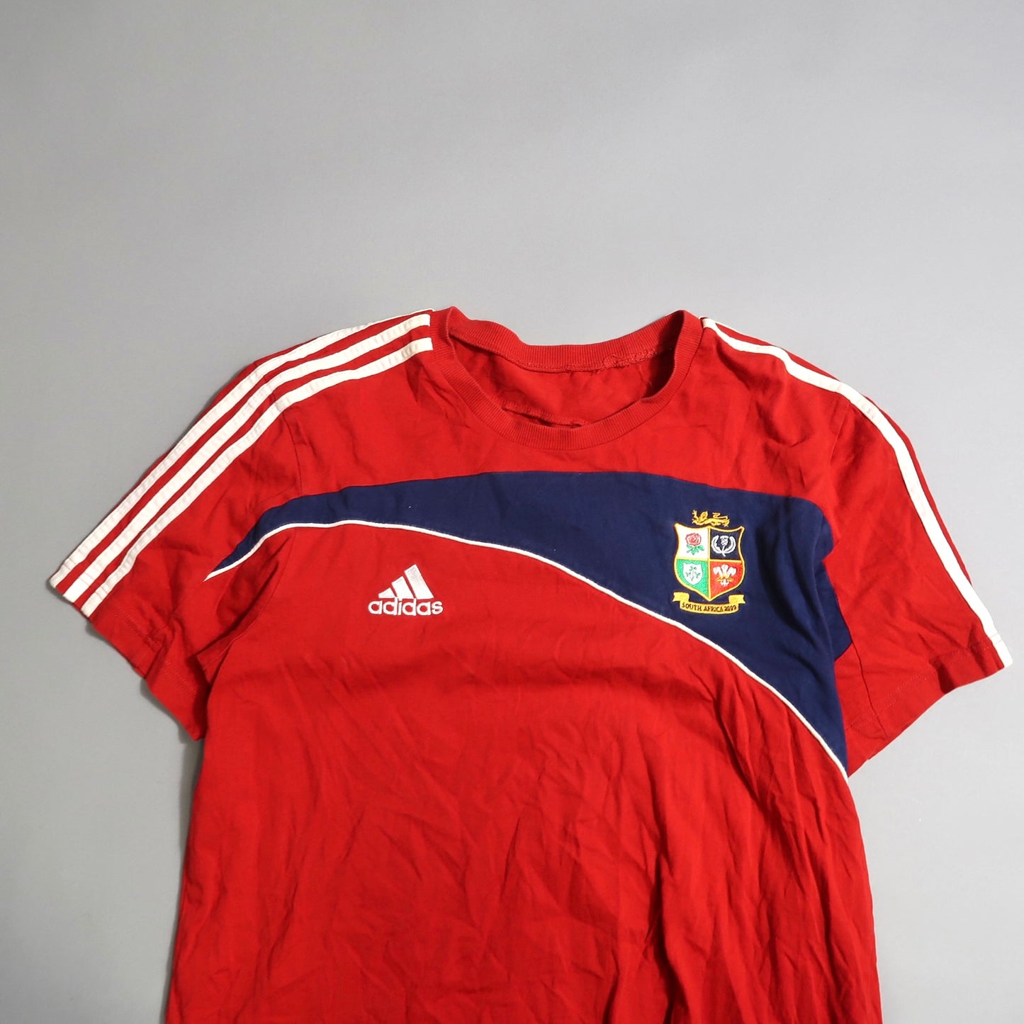 Red Adidas shirt with sports emblem and white stripes.