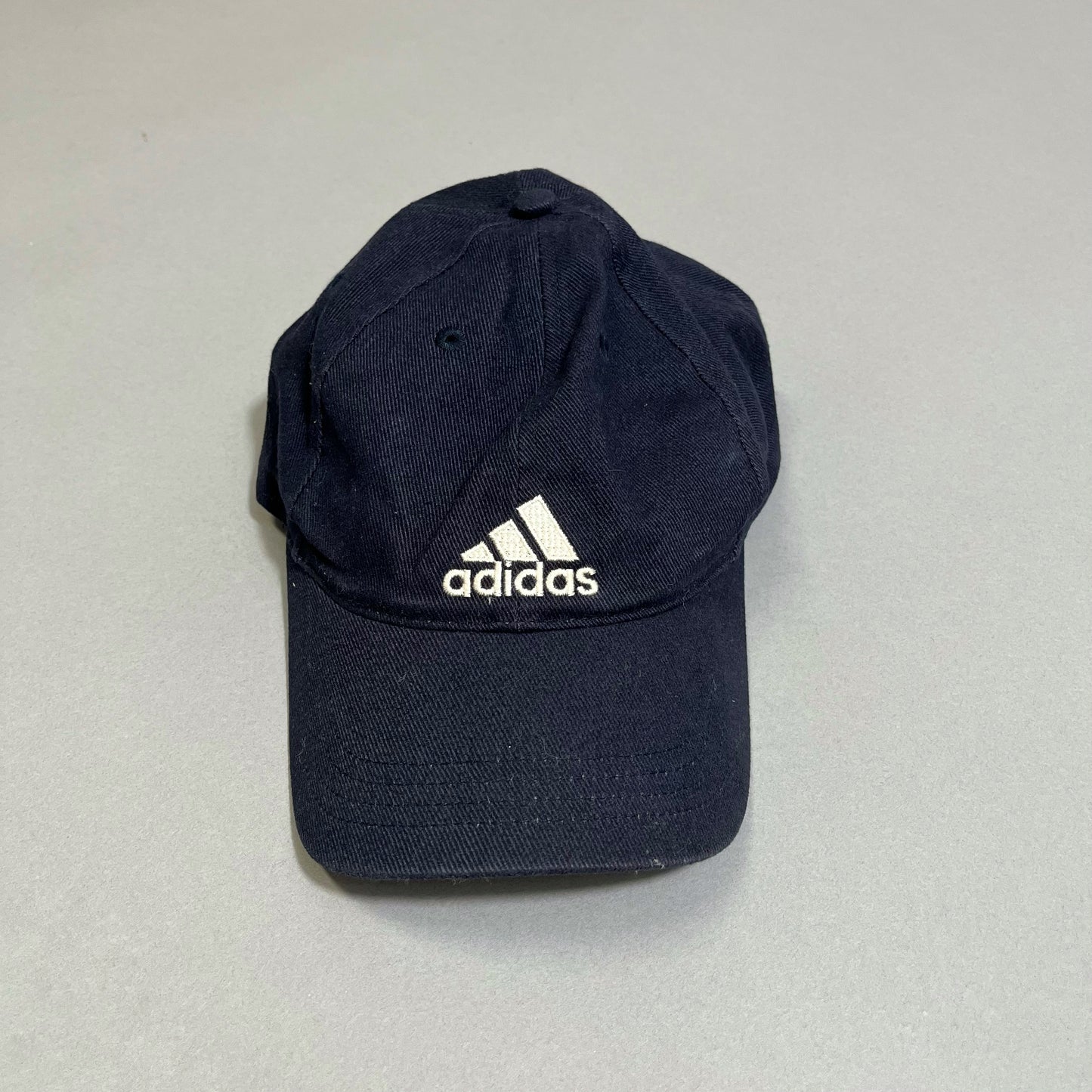 Black Adidas cap with white logo on gray background.