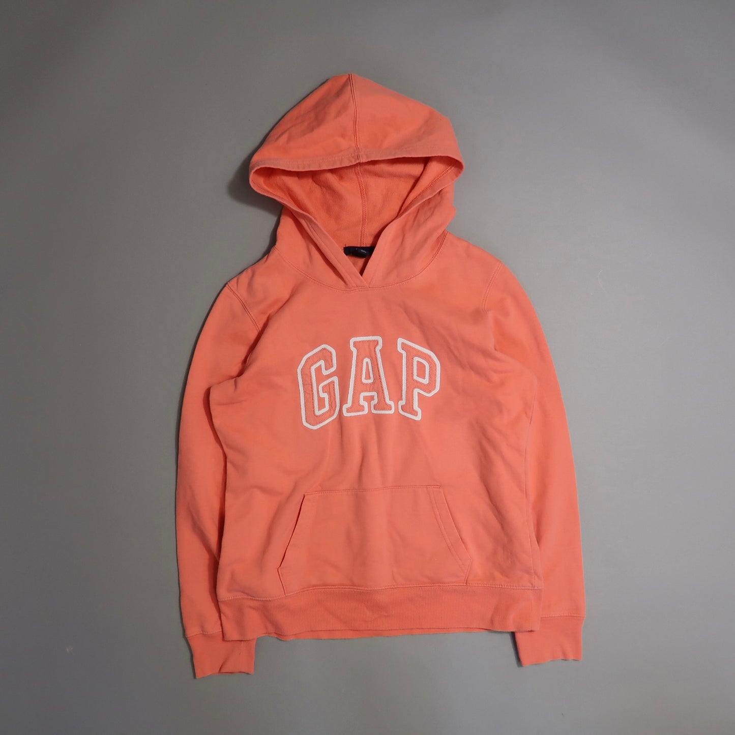 Orange GAP hoodie with front pocket on a gray background.