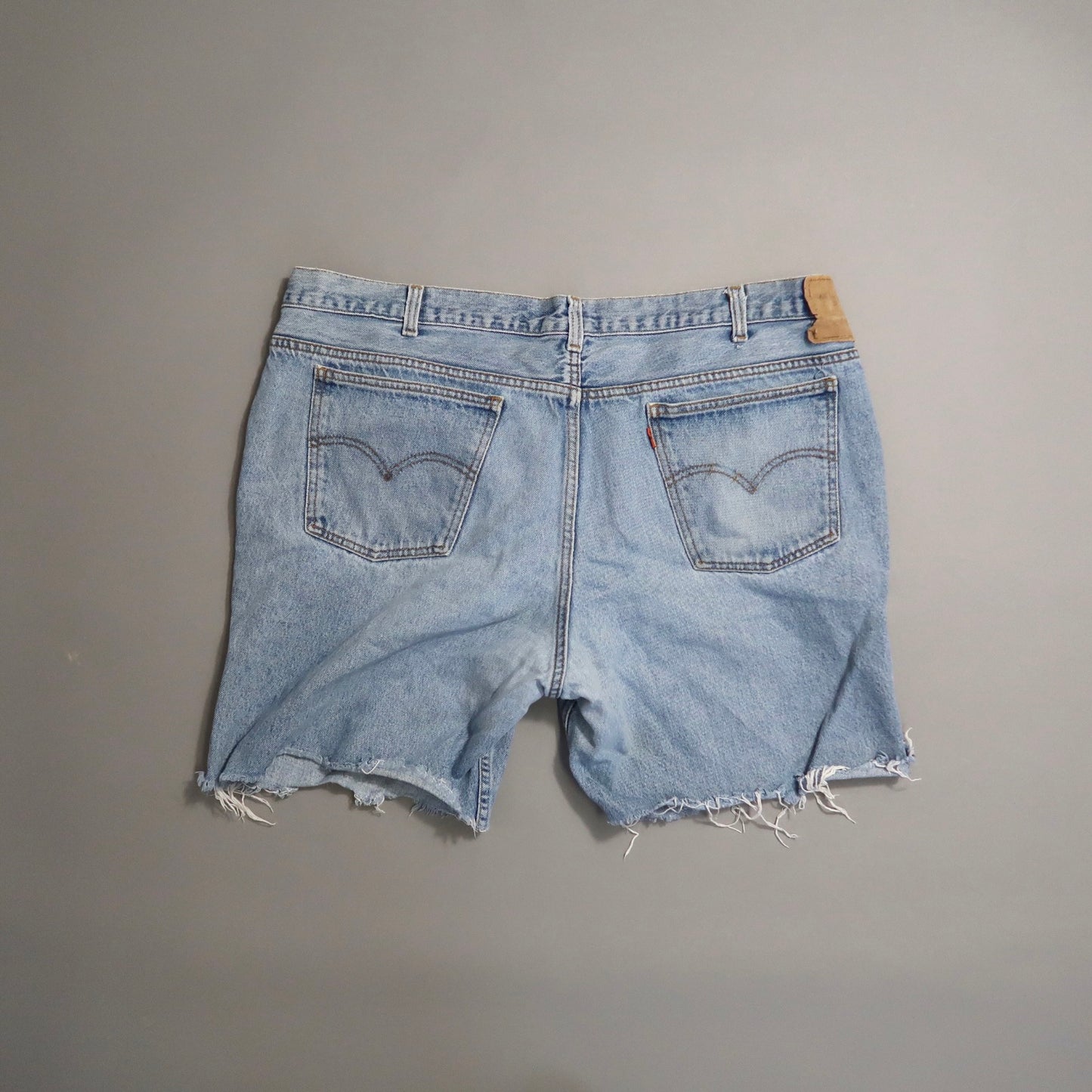 Frayed edge denim shorts with back pockets on a neutral background.