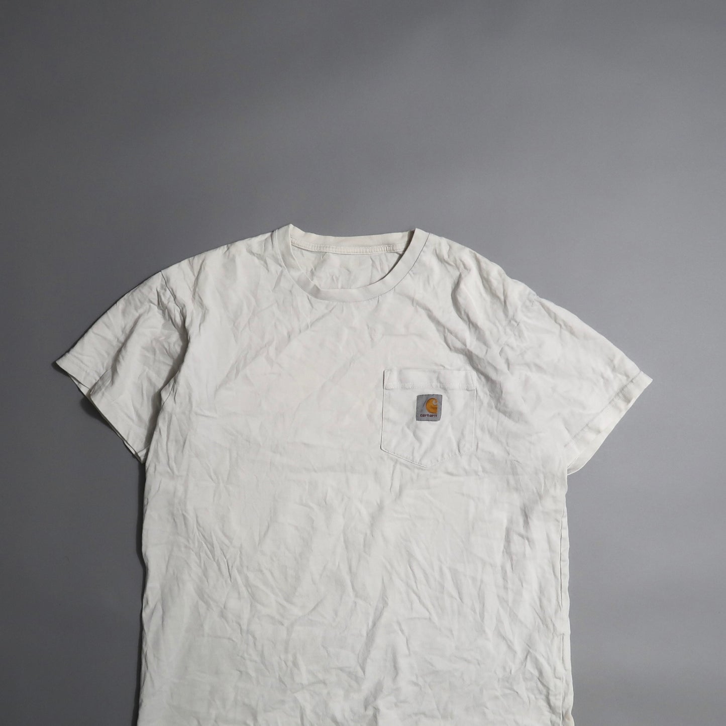 Crumpled white T-shirt with logo on pocket, against gray background.