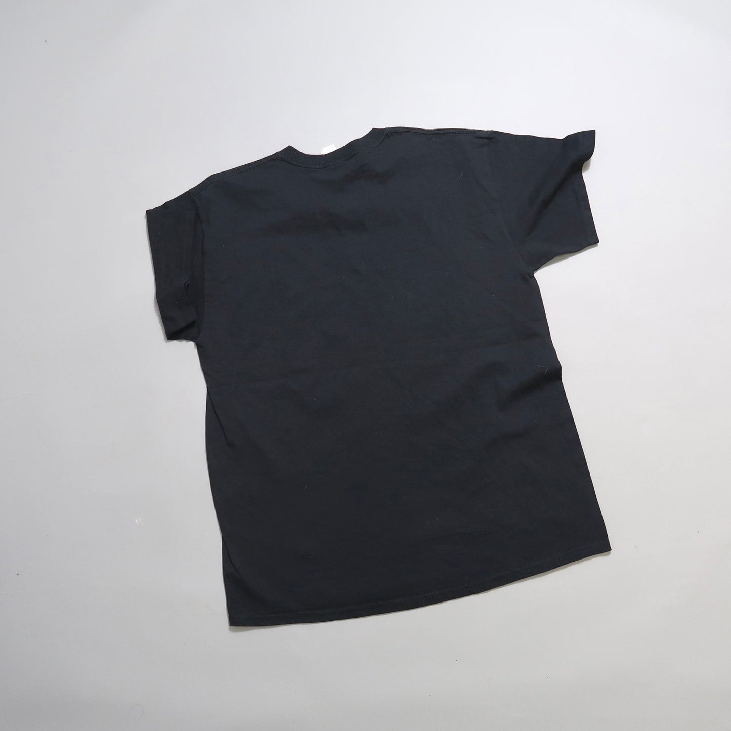 A plain black T-shirt laid flat on a light gray background.