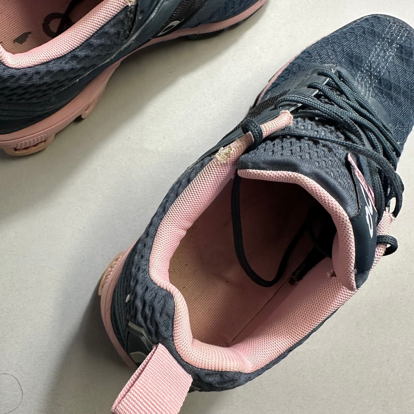 Worn dark blue sneakers with pink interiors on a light surface.