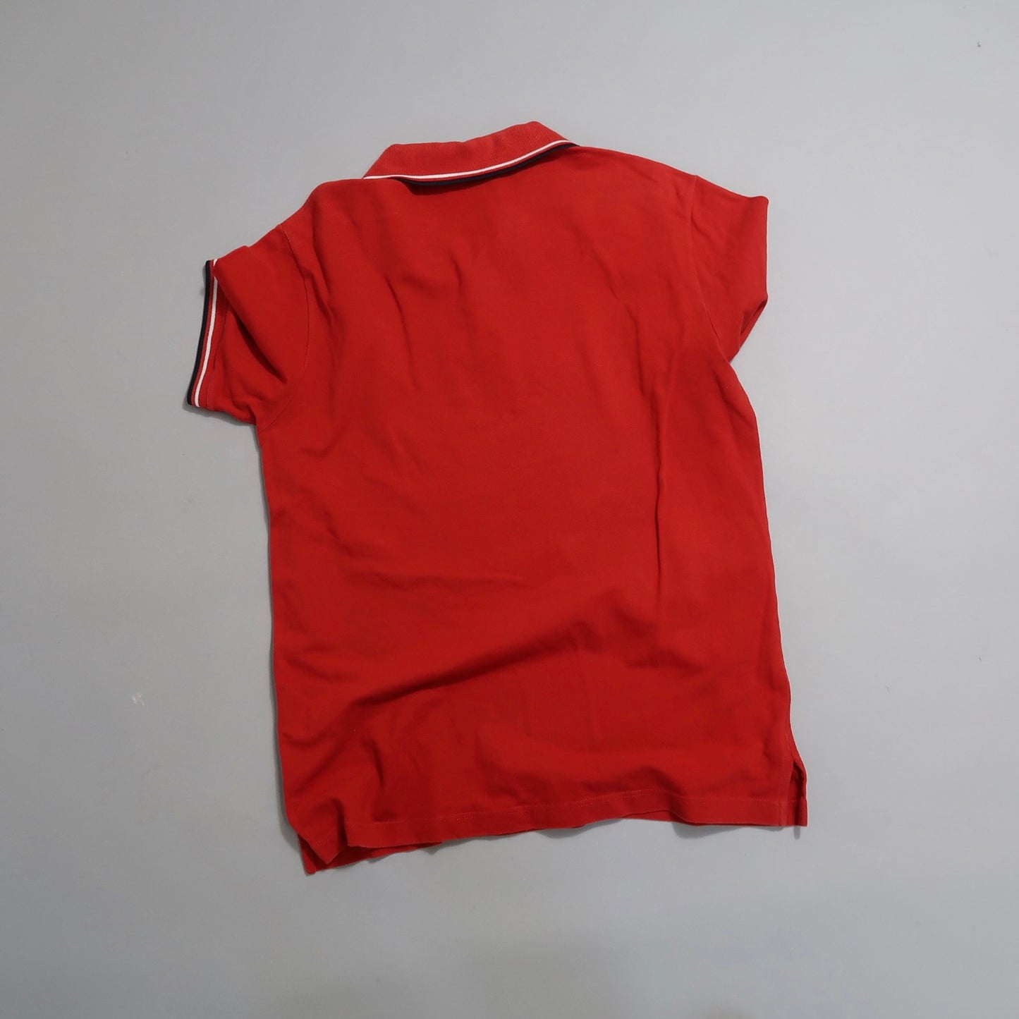 Red polo shirt with white and black collar stripe on a gray background.