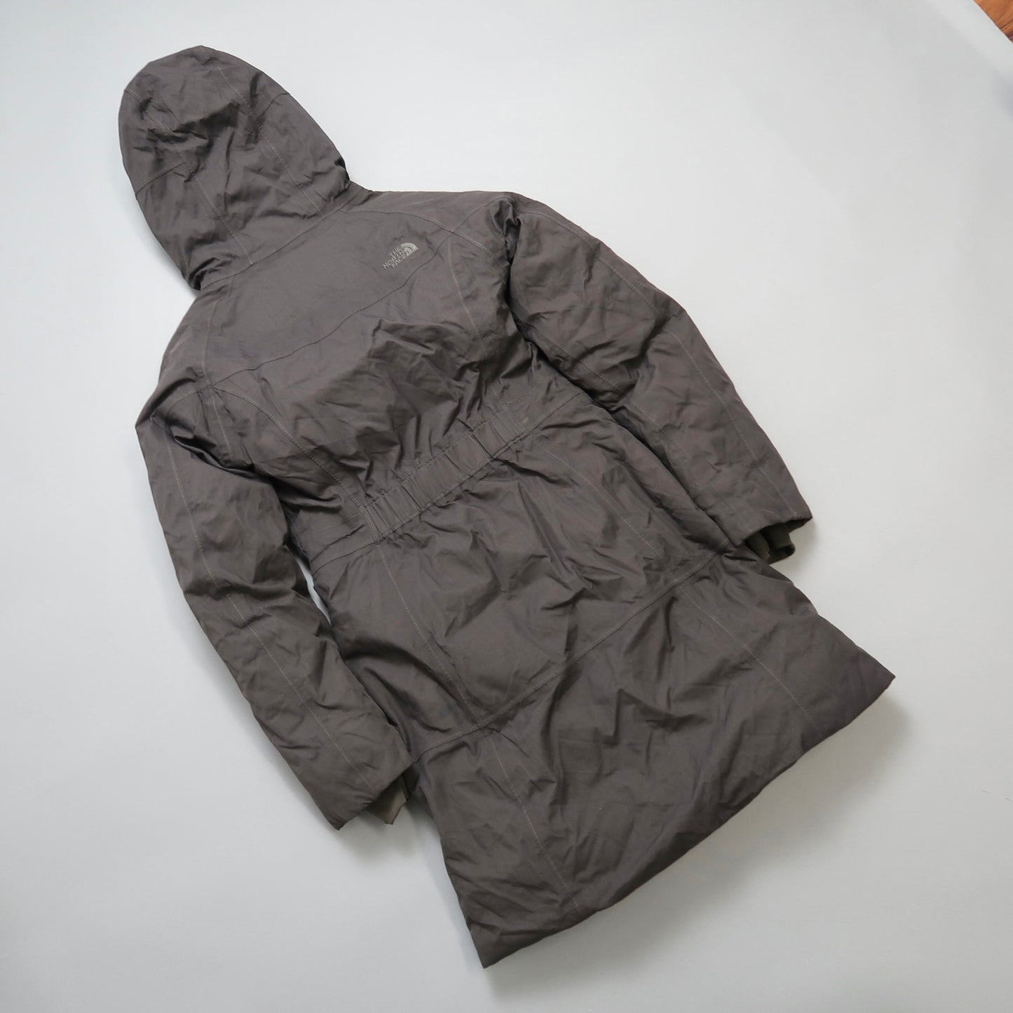 Gray hooded winter coat on a flat surface, rear view.
