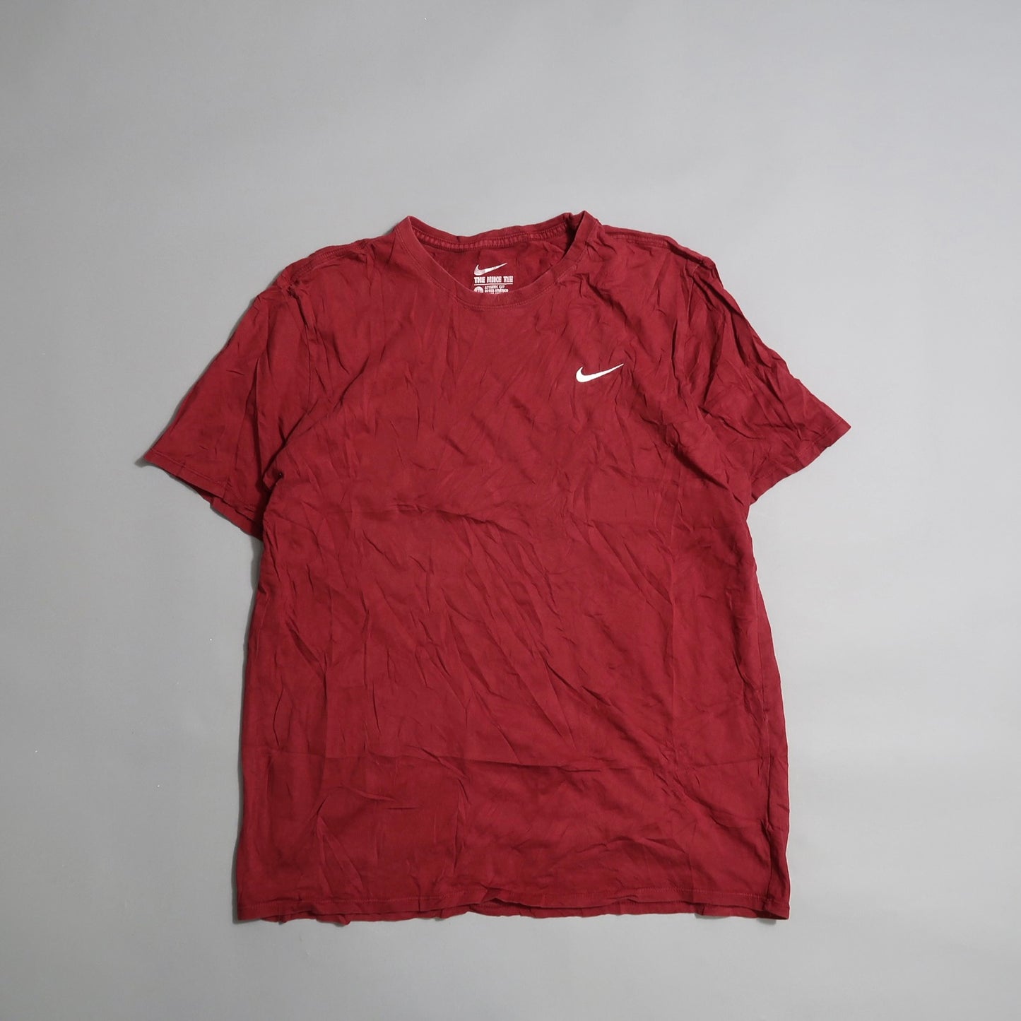 Wrinkled red T-shirt with a white swoosh logo on a gray background.