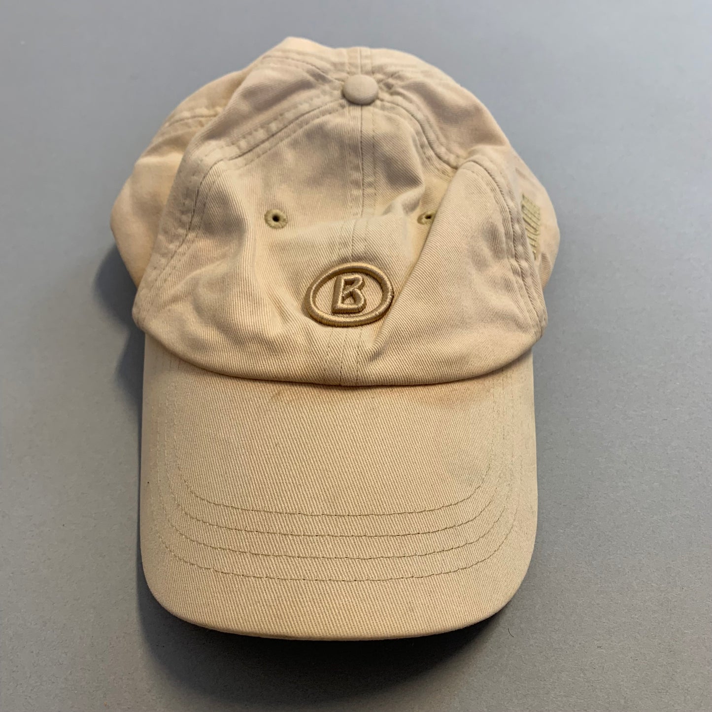 Beige baseball cap with a nullBnull logo on the front, placed on a table.