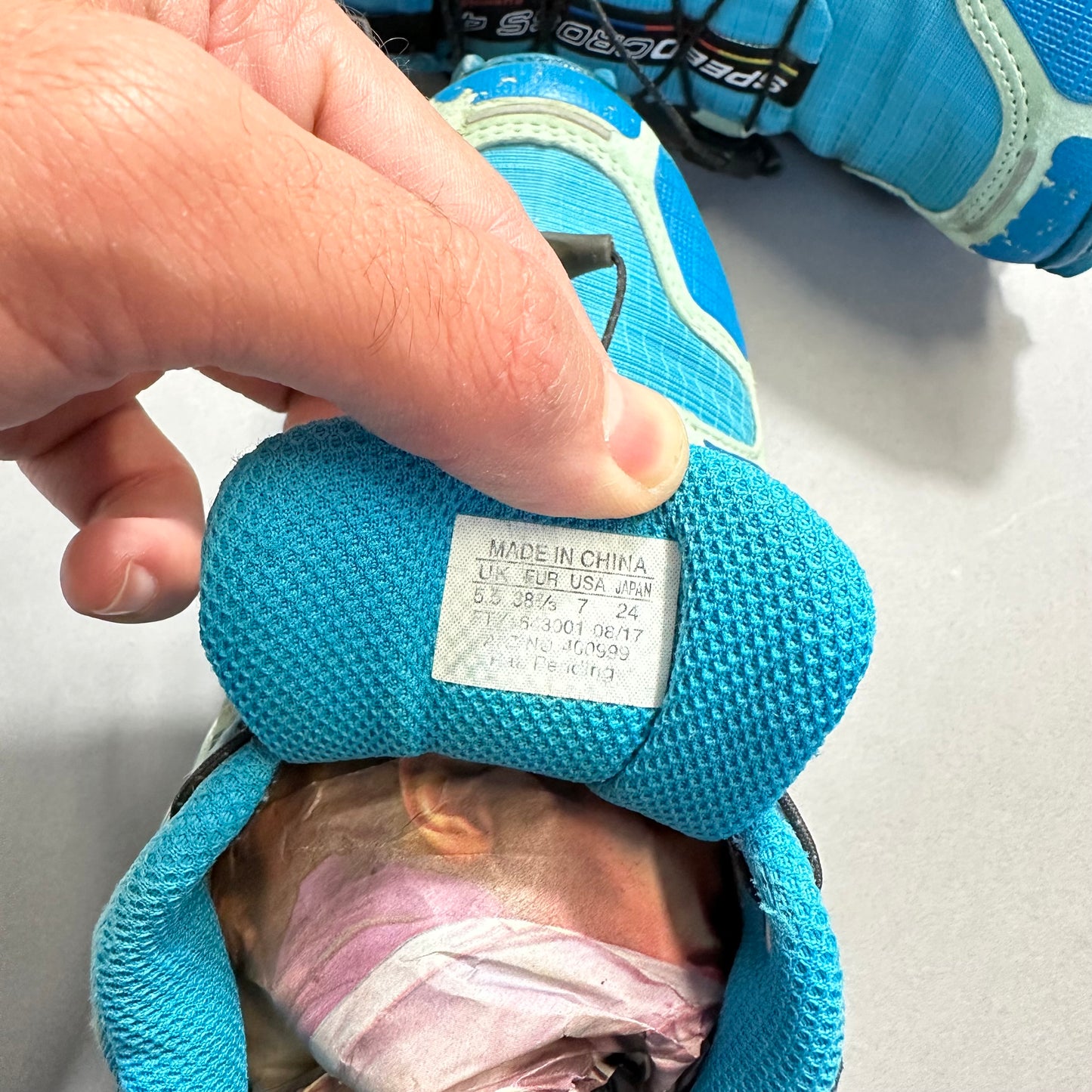 Hand holding a blue shoe with visible size tag inside.
