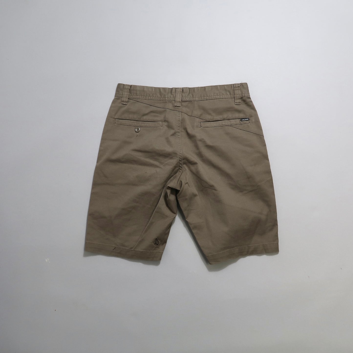 Back view of beige shorts with back pockets on a flat surface.