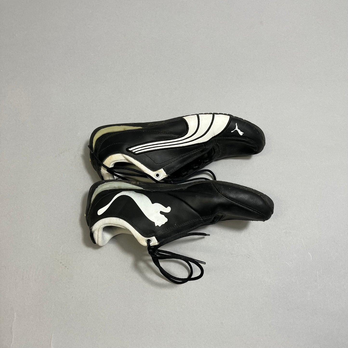 Black racing shoes with white logo and design, laces untied.