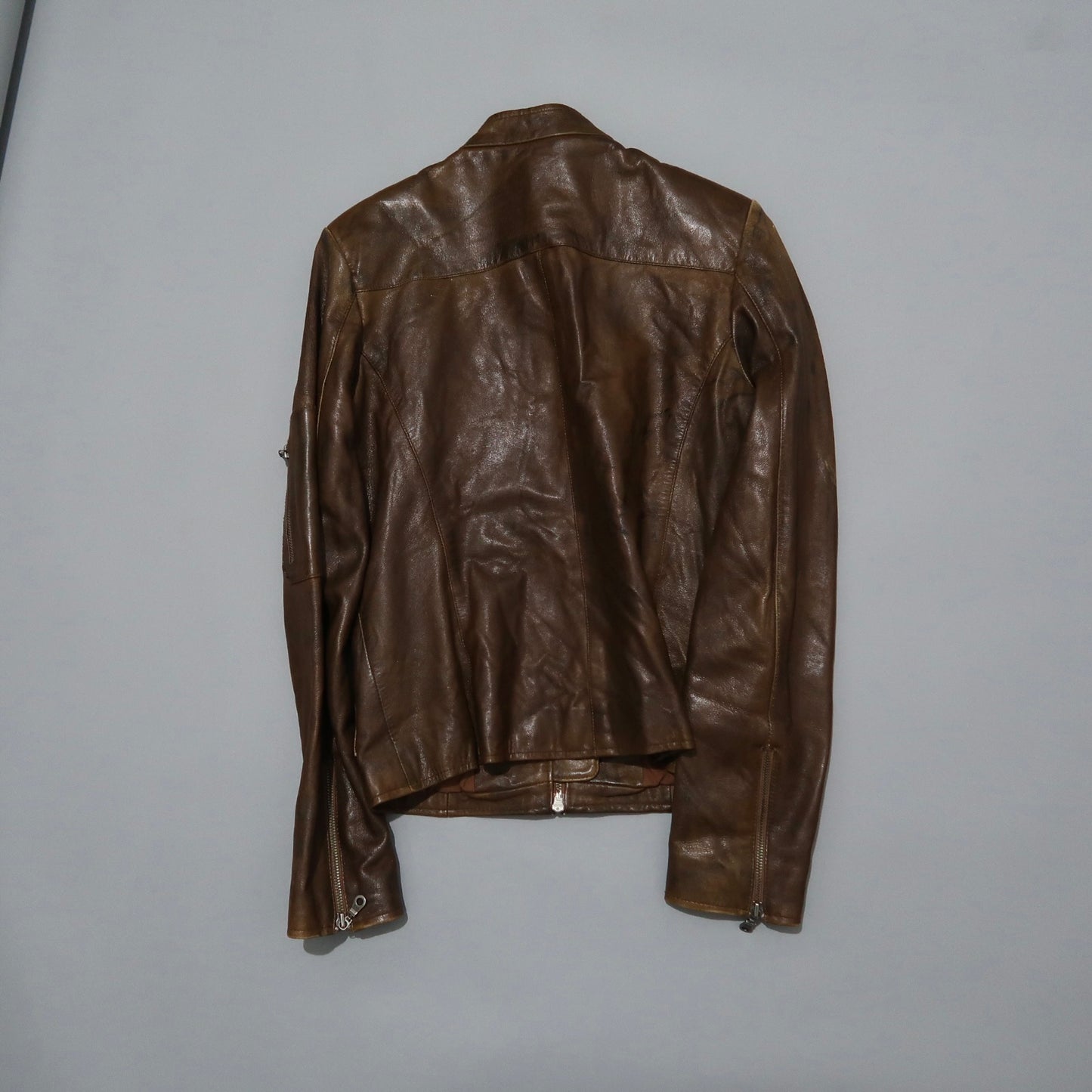 Brown leather jacket hung on a light gray background.