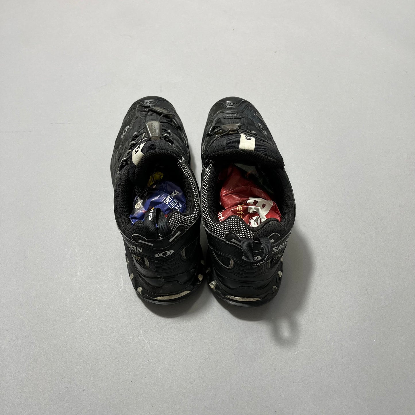 Black shoes stuffed with colorful crumpled paper on a gray surface.