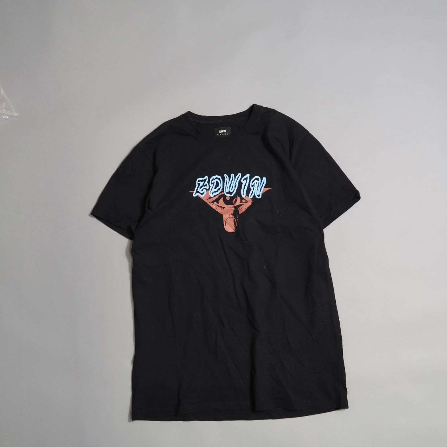 Black T-shirt with nullEDWINnull and artwork on the front, laid on gray surface.