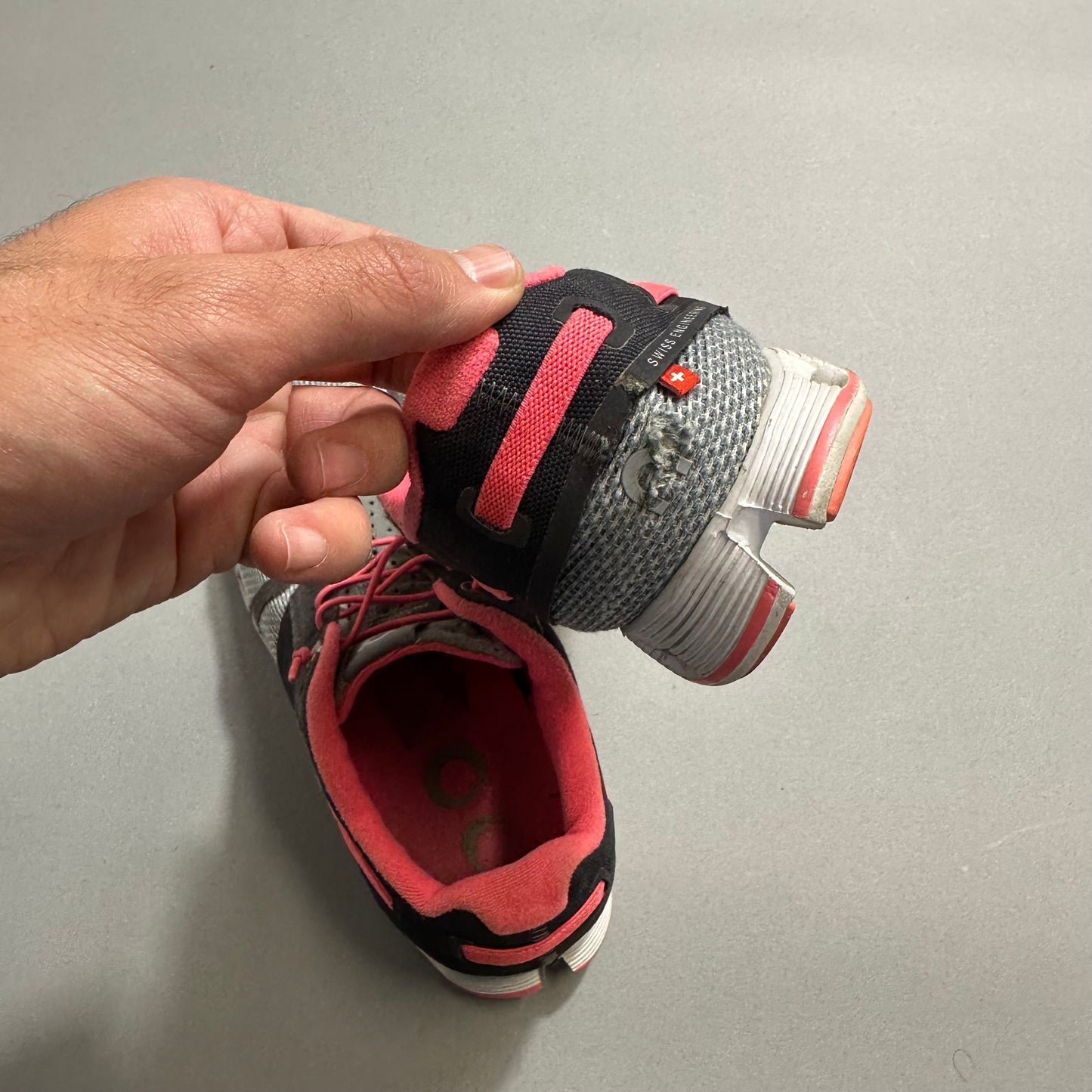 Hand holding a torn pink and gray athletic shoe.
