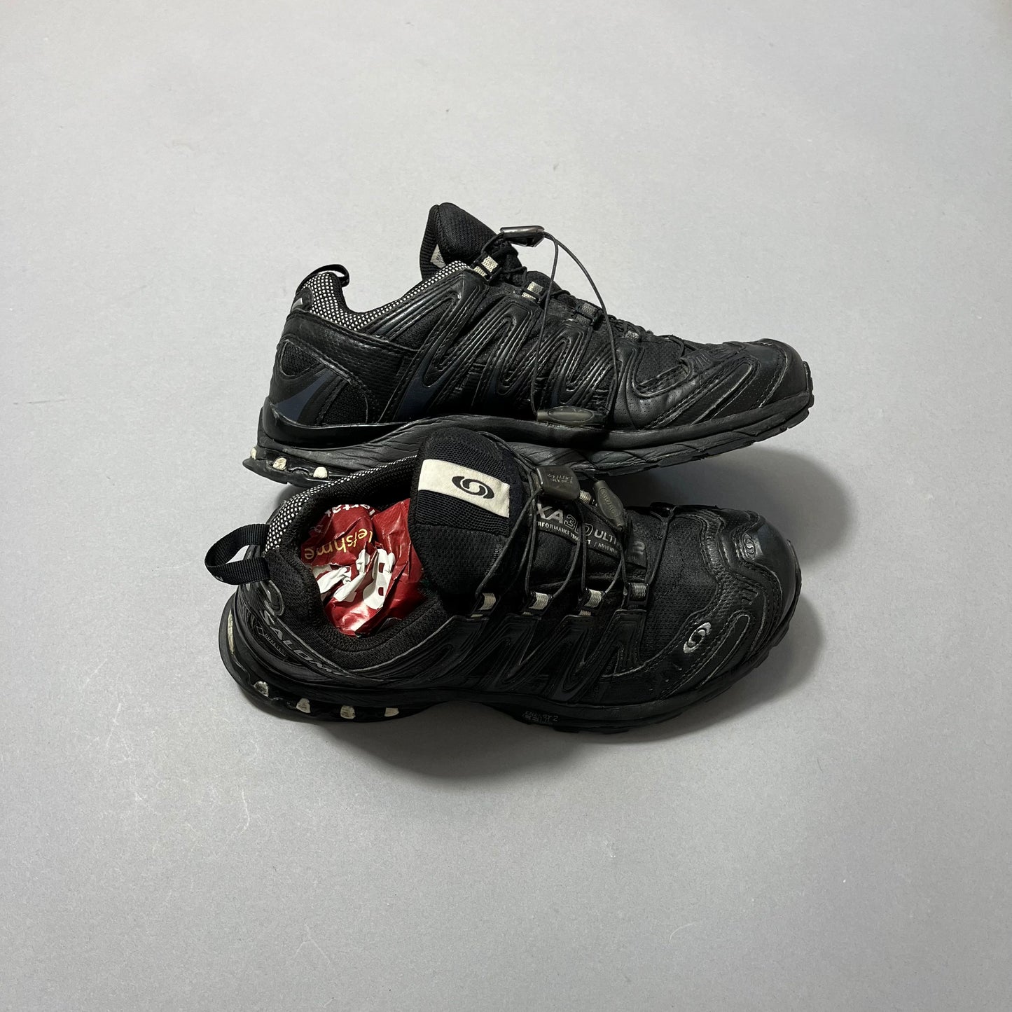 Black sneakers with a red packet inside one shoe.