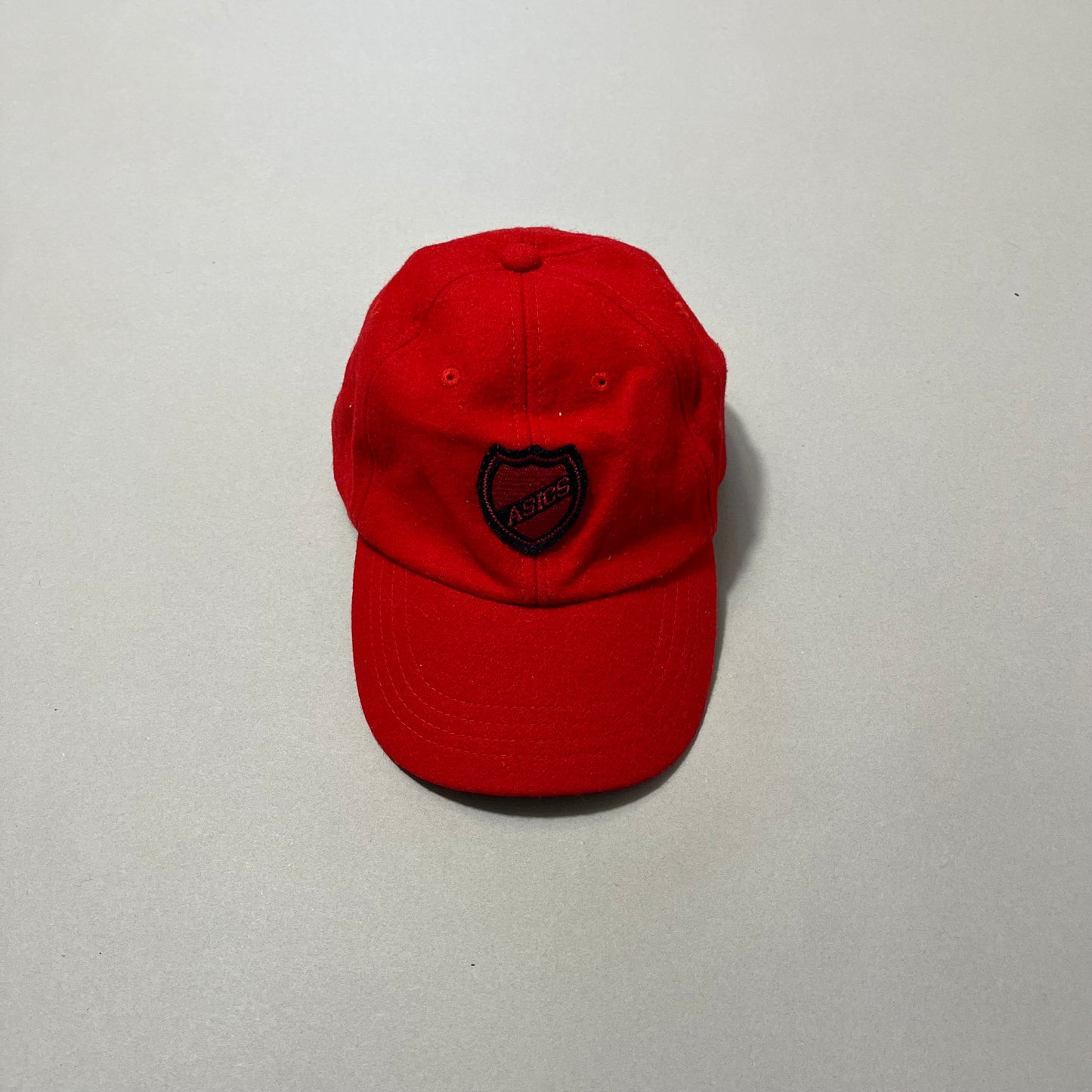 Red cap with embroidered nullASICSnull logo on a neutral background.