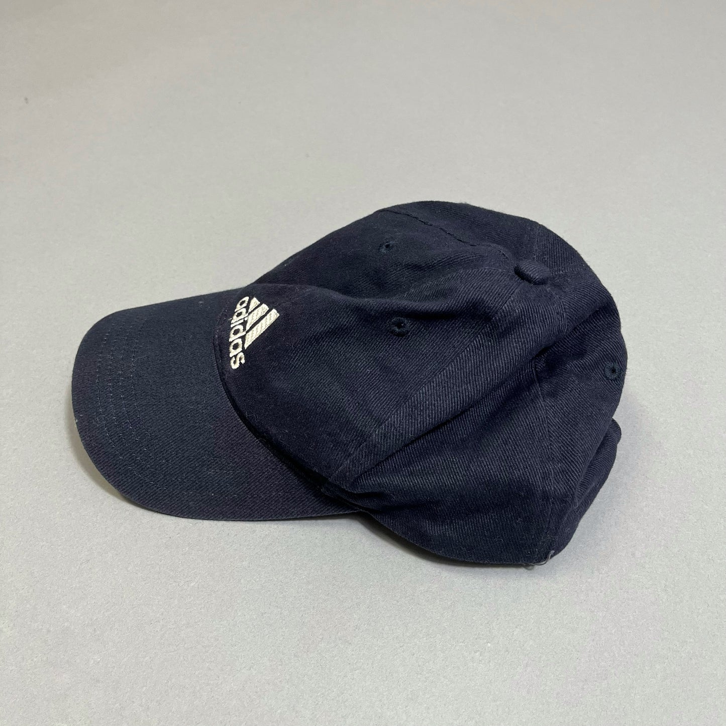 Black Adidas cap with white logo on a gray surface.