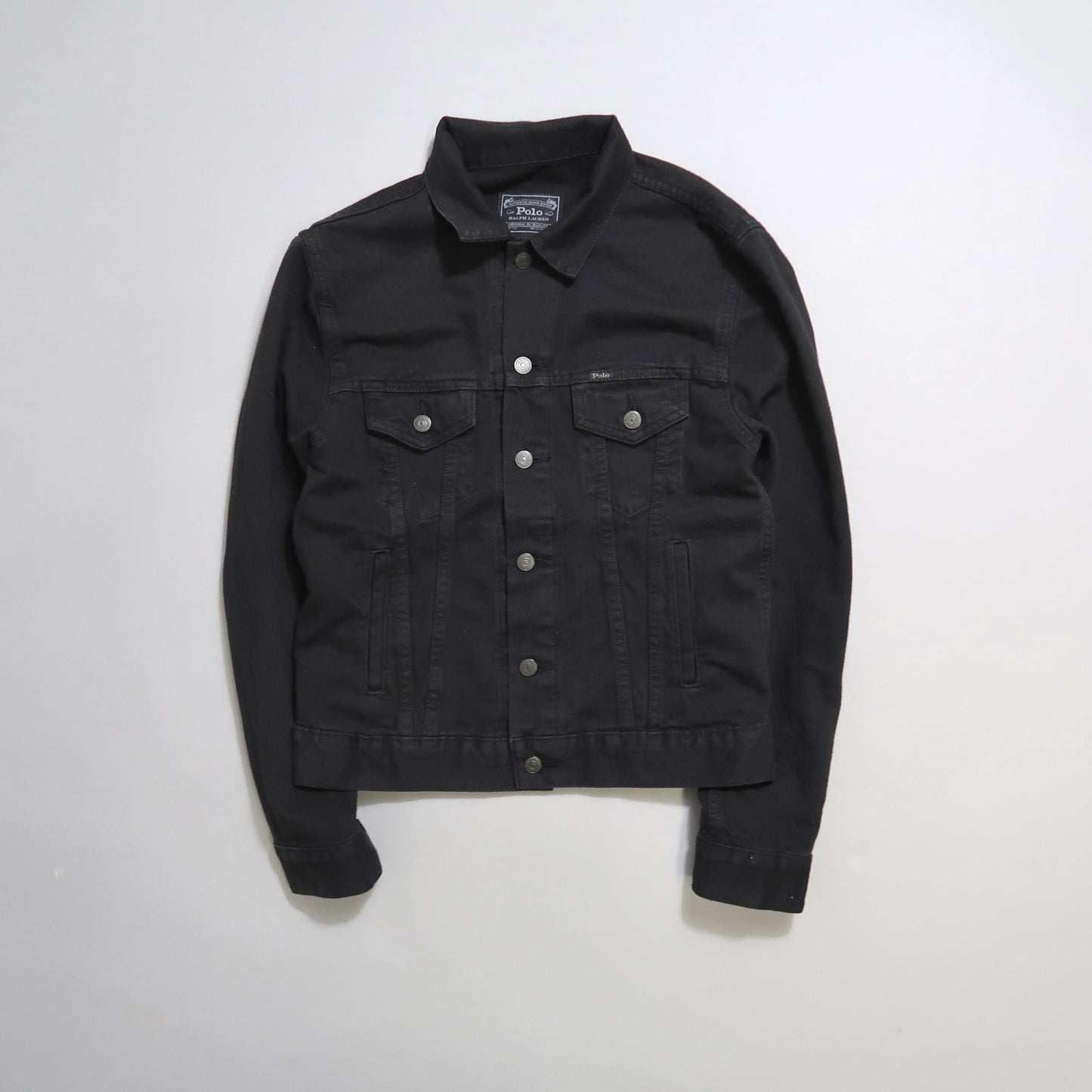 Black denim jacket with silver buttons on a white background.