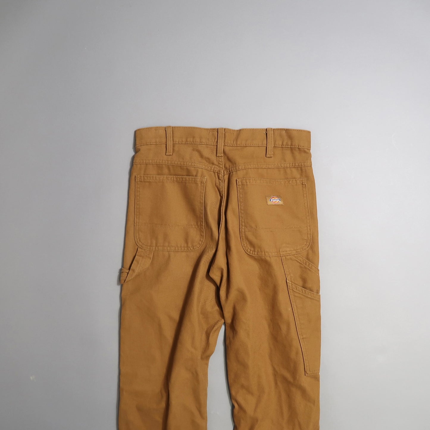 Brown work pants with back pockets on a gray background.