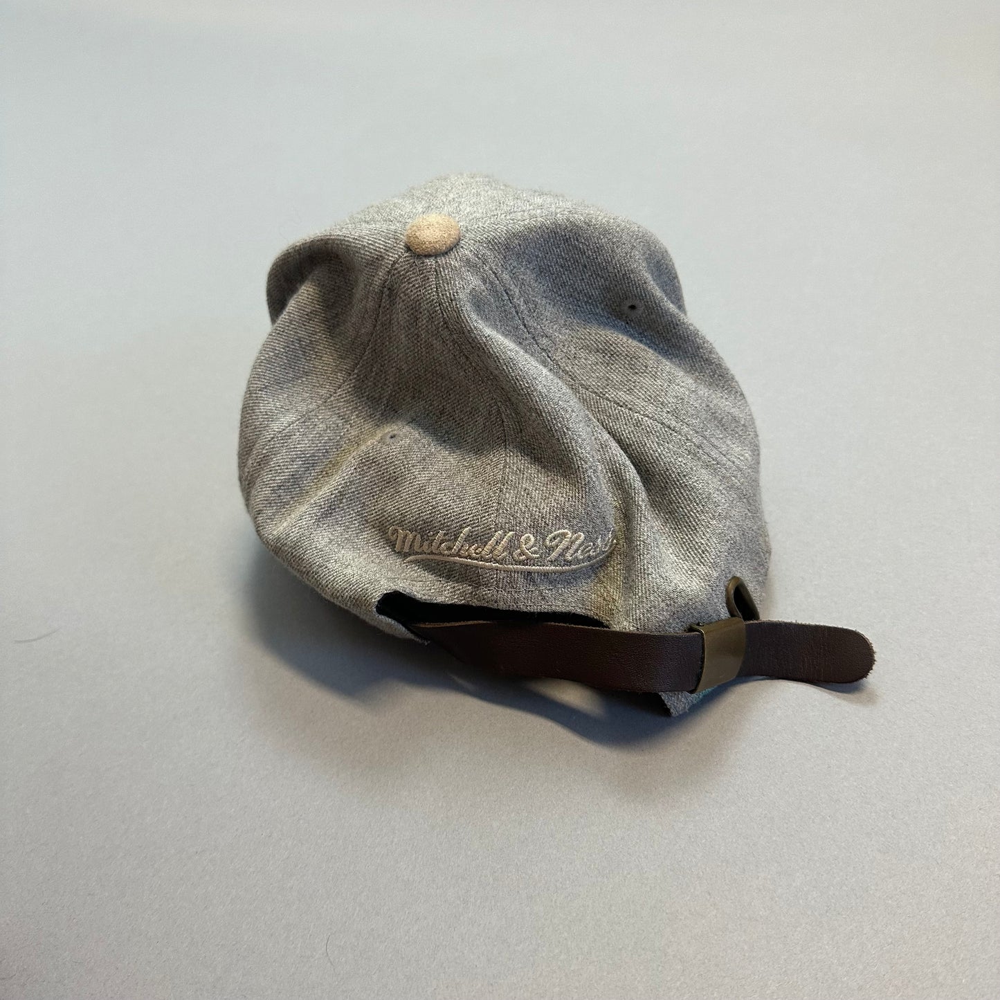 Gray Mitchell & Ness cap with adjustable strap on a flat surface.