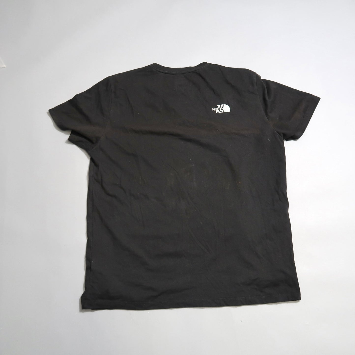 Black T-shirt with a small logo on the back, displayed on a flat surface.