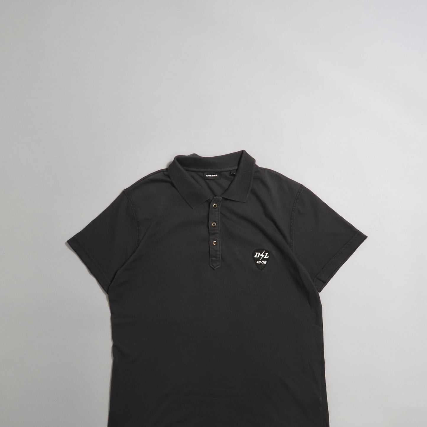 Black polo shirt with a logo on the chest, displayed on a gray background.