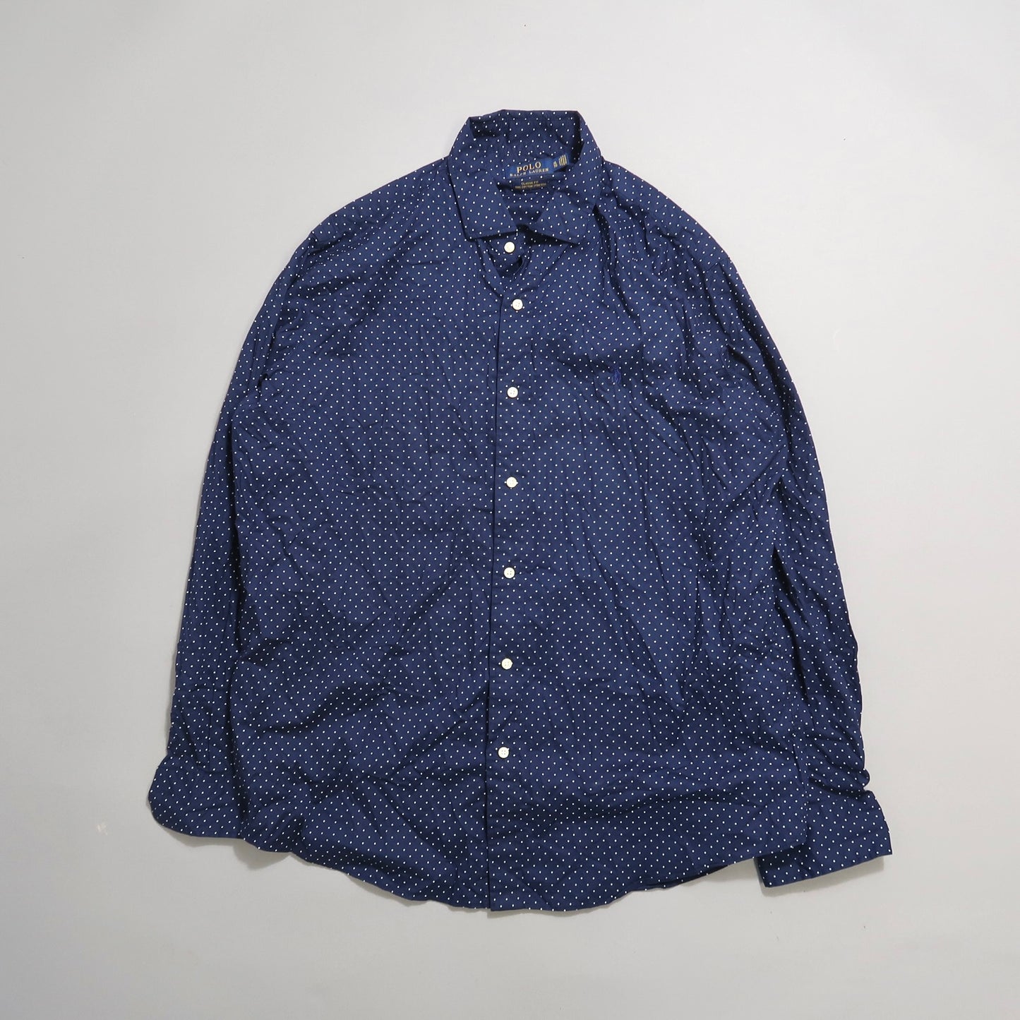 Navy blue polka dot button-up shirt on a plain background.