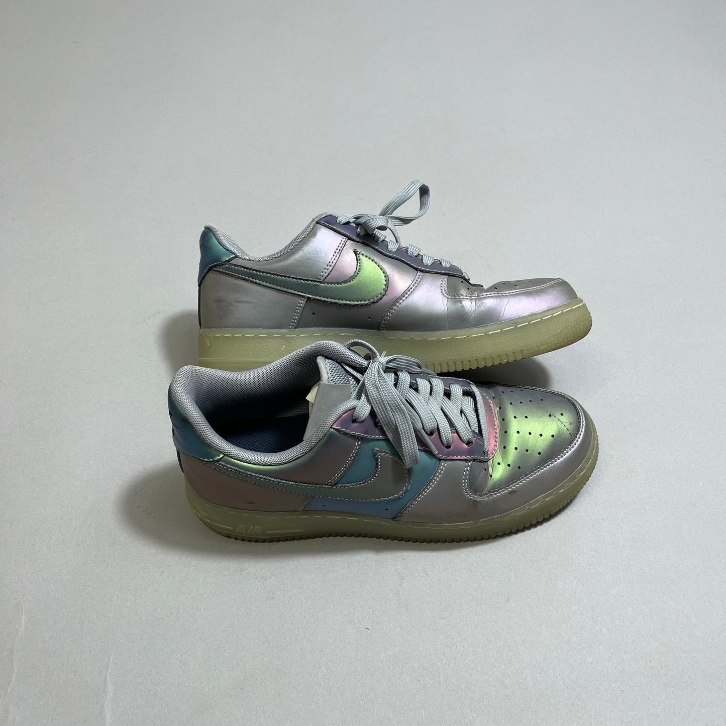 Iridescent sneakers with grey laces on a plain background.