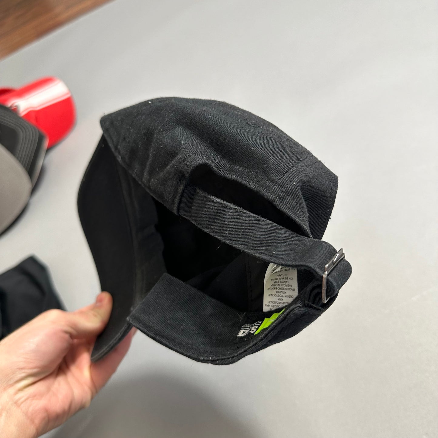 Black cap with adjustable strap held in a person's hand.