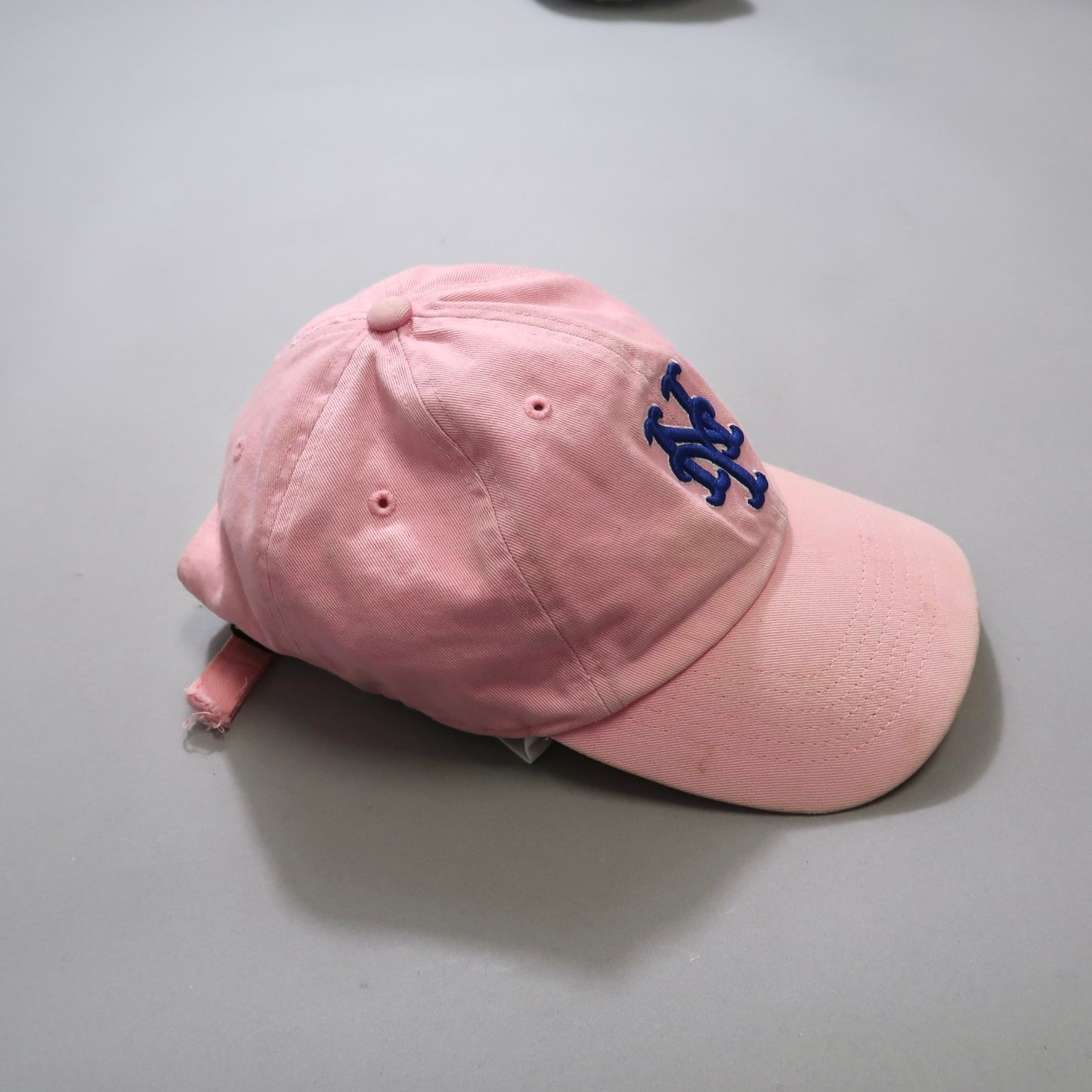 Pink baseball cap with a blue embroidered logo on a gray background.
