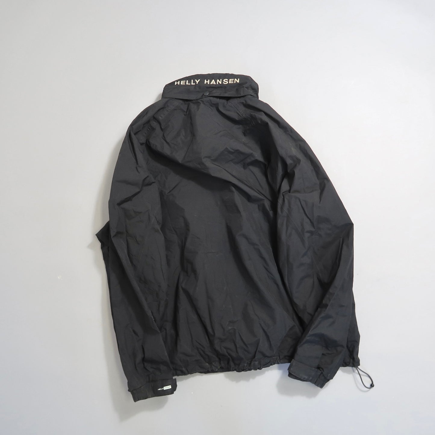 Black Helly Hansen jacket laid flat, showing back with logo collar.