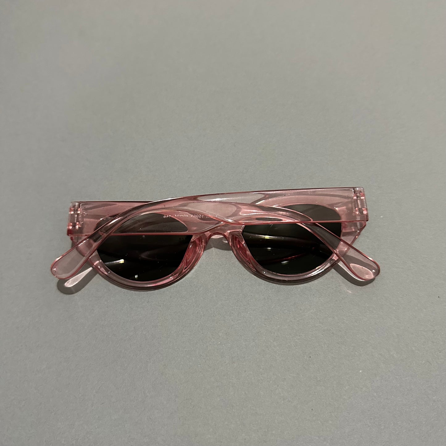 Folded pink sunglasses with black lenses on a gray surface.