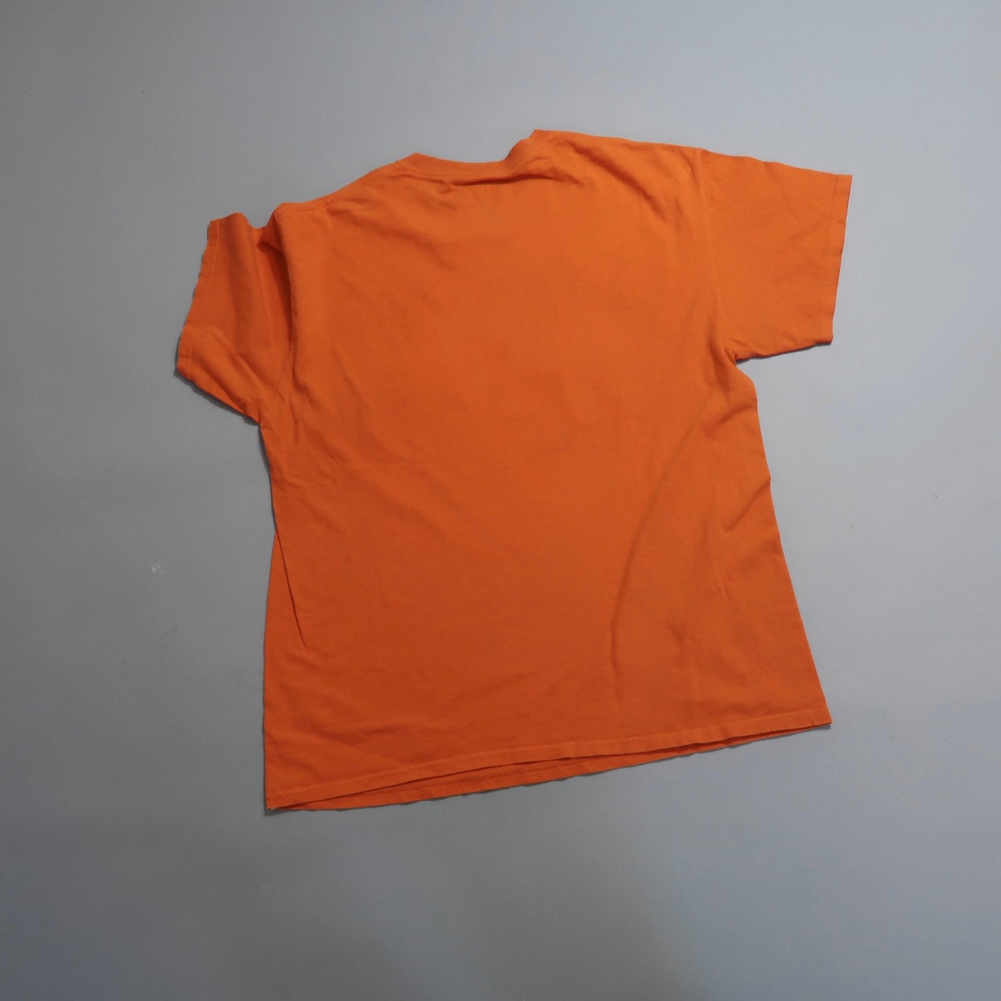Orange T-shirt laid flat on a gray surface, viewed from the back.