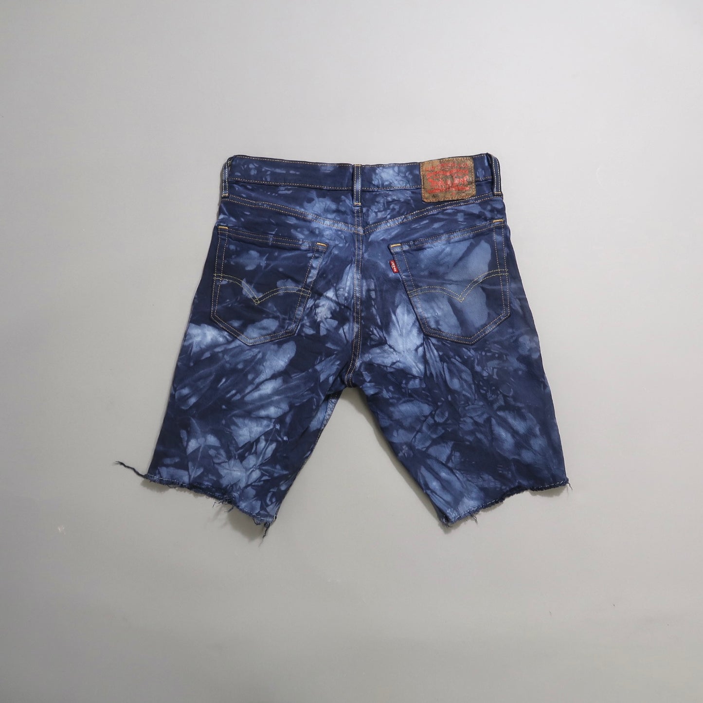 Blue tie-dye denim shorts, back view with visible pockets.