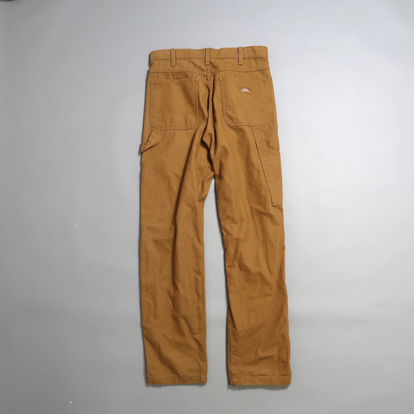 Brown work pants with multiple pockets, laid flat on a gray surface.