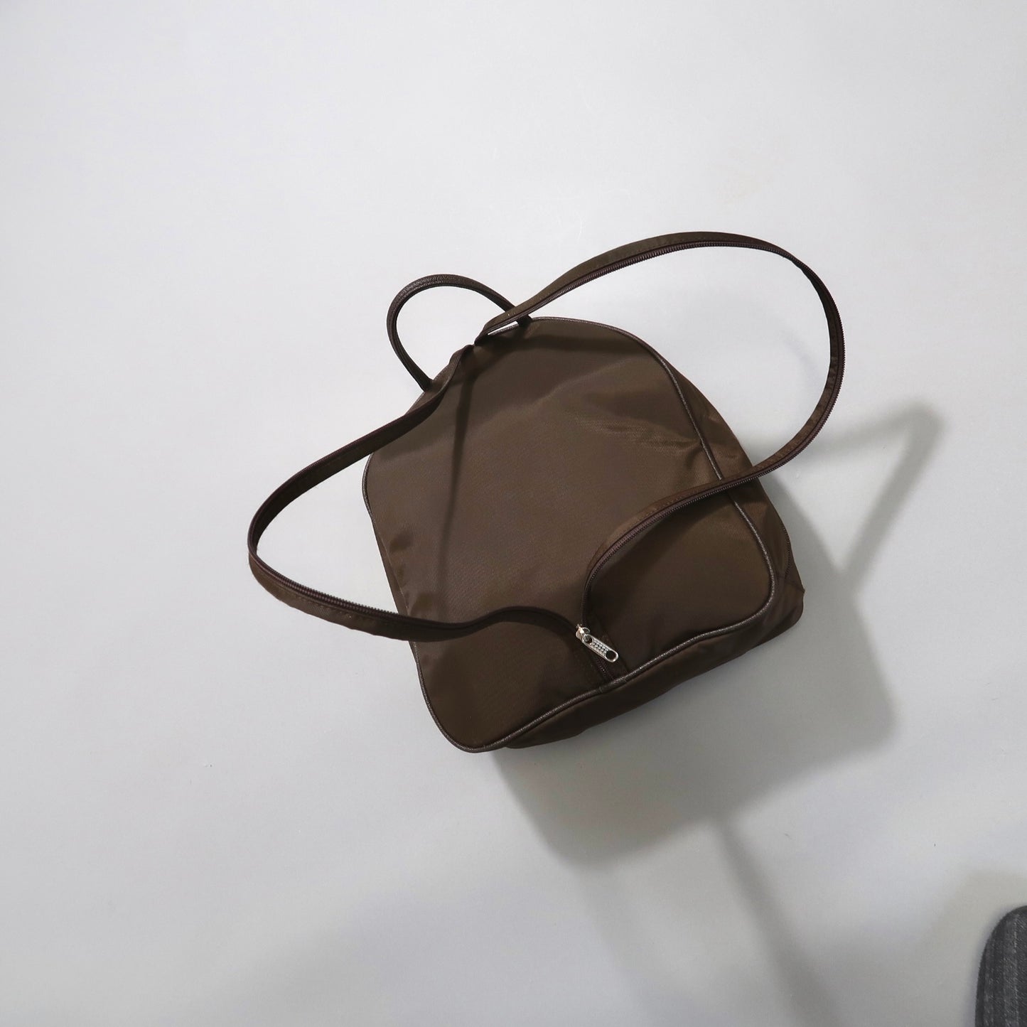 Brown tote bag with a zipper, lying on a light surface.