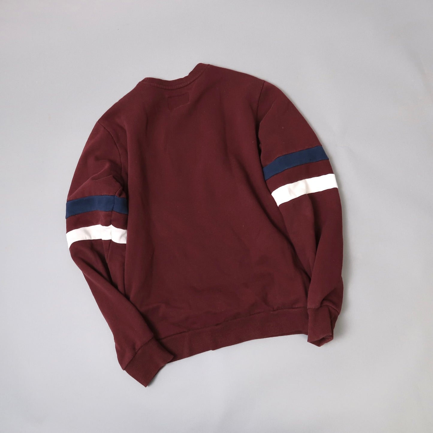 Maroon sweatshirt with blue and white striped sleeves on gray background.