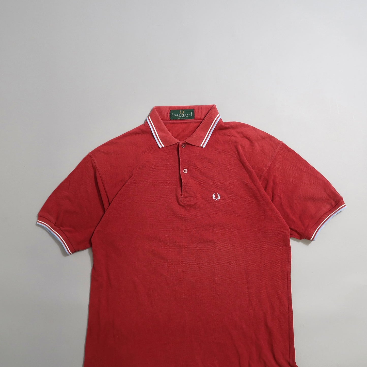 Red polo shirt with white trim and a laurel wreath logo on the chest.